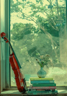A cozy corner with a violin resting on a wooden chair beside colorful music books and soft natural light.