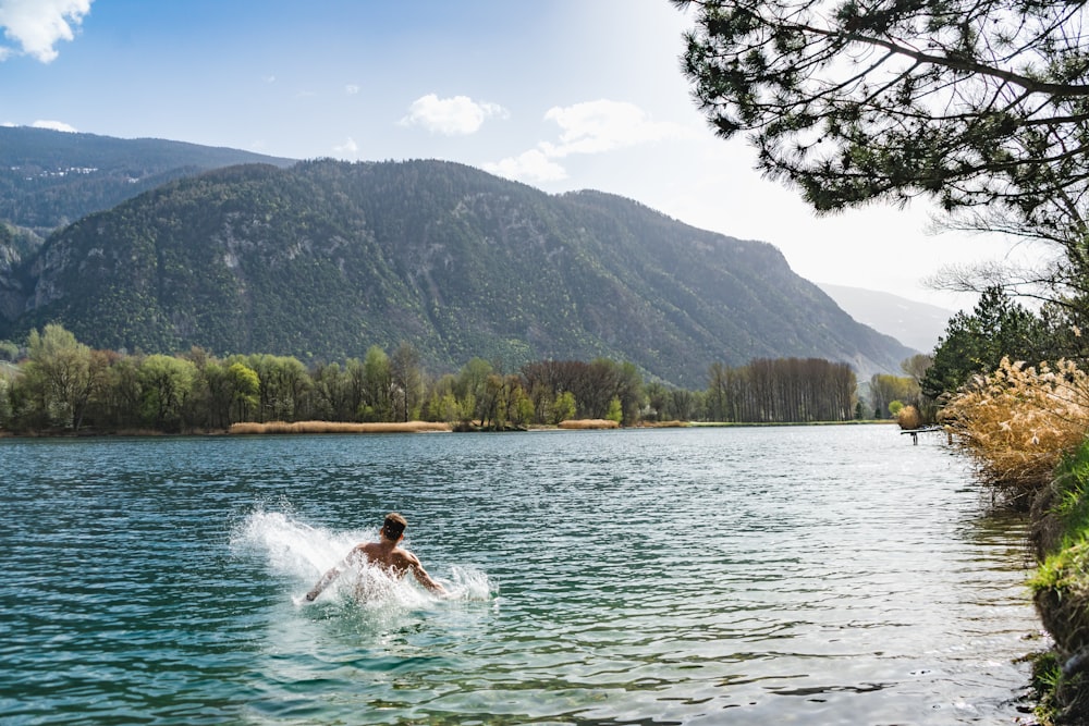 woman in white dress on water near green trees and mountain during daytime