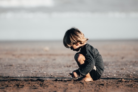 girl in gray hoodie sitting on brown sand during daytime