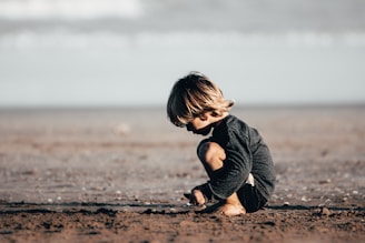 girl in gray hoodie sitting on brown sand during daytime