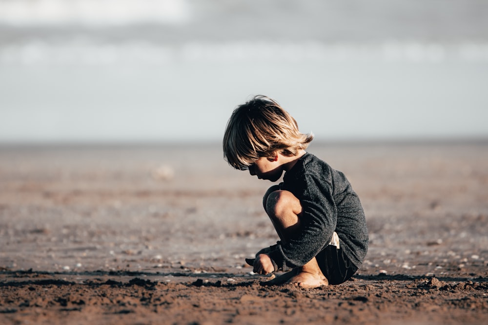 menina no capuz cinza sentado na areia marrom durante o dia