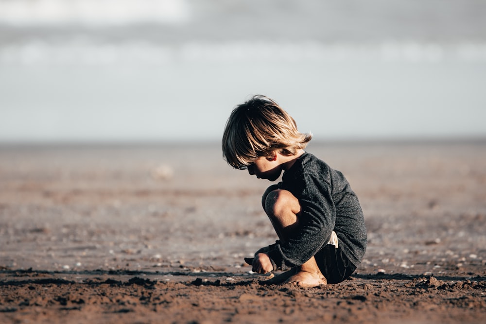 girl in gray hoodie sitting on brown sand during daytime