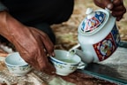 person holding white and red floral ceramic teapot