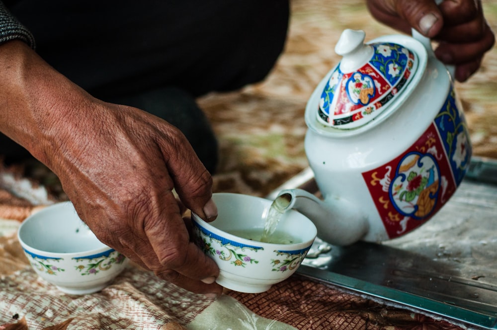 person holding white and red floral ceramic teapot