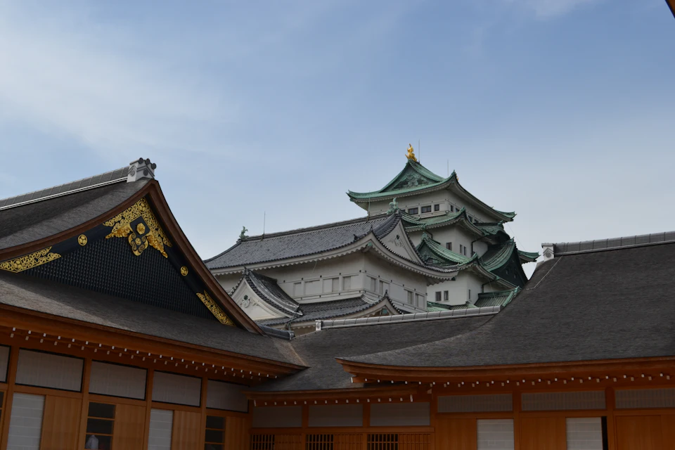 The image depicts a traditional Japanese temple with three distinct towers, each adorned with gold accents and intricate designs. The temple is situated within a courtyard surrounded by wooden buildings, creating an atmosphere of cultural heritage and architectural beauty. The sky above is clear blue, providing a serene backdrop to the scene.