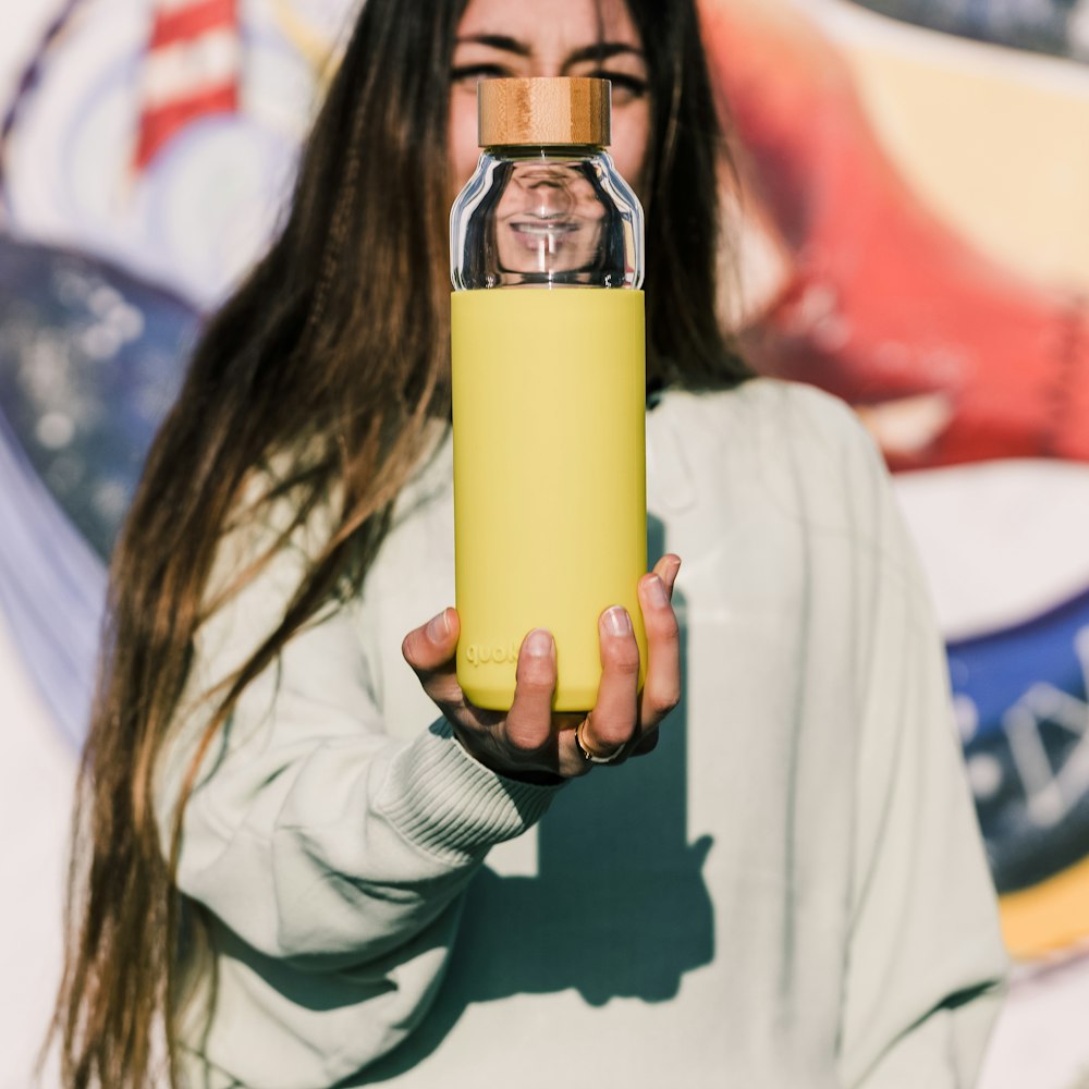 woman in white long sleeve shirt holding yellow and silver tumbler