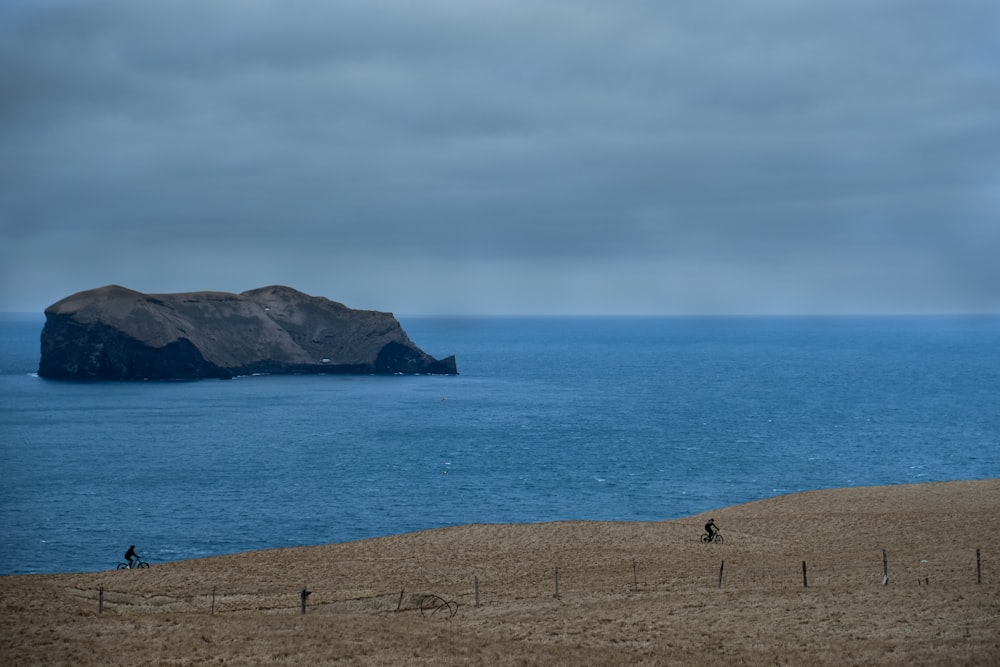 pessoa em pé na areia marrom perto do corpo de água durante o dia