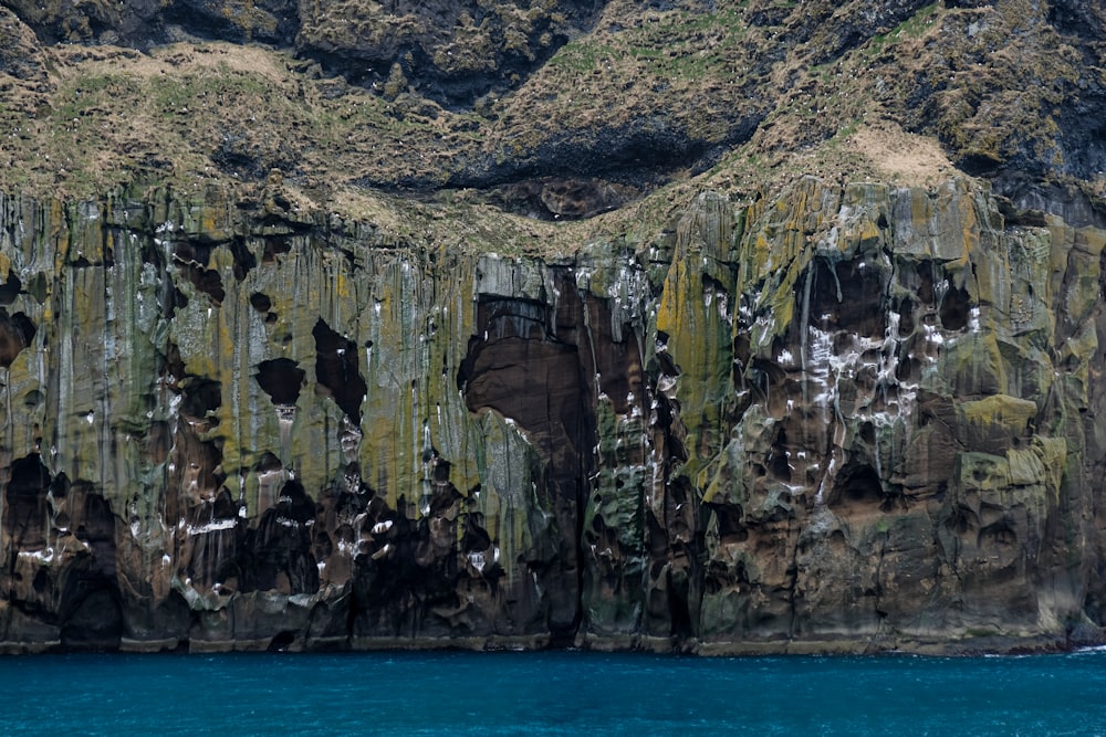 brown and green rock formation beside blue sea during daytime