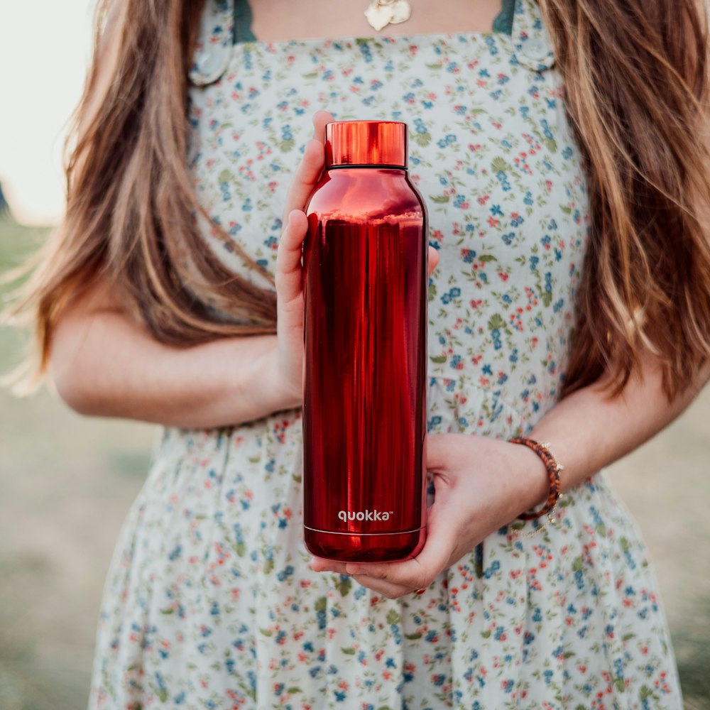 woman in white and pink floral dress holding red bottle