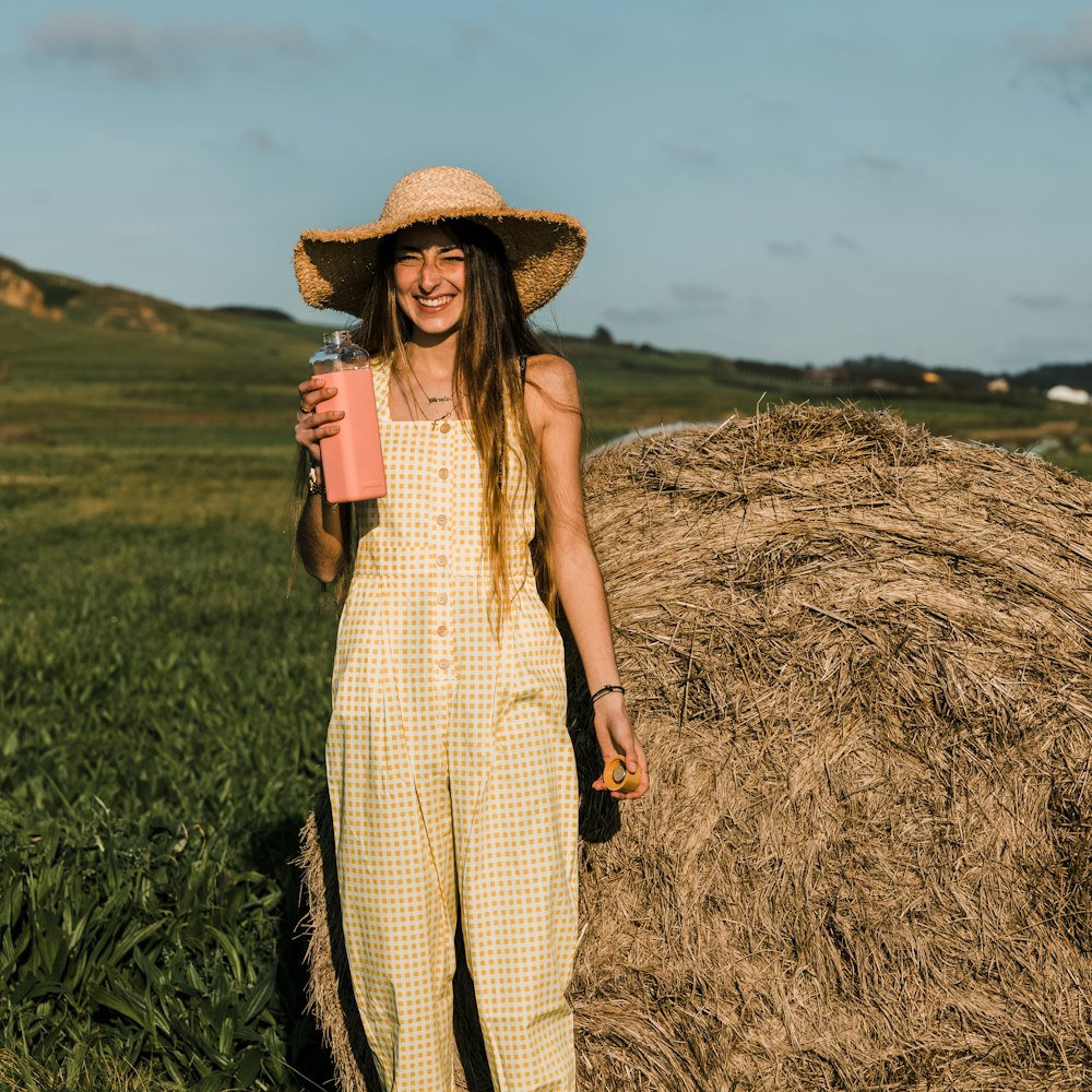 woman in brown and white plaid dress wearing brown straw hat standing on brown grass field