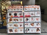 A display stand showcasing various 2020 calendars featuring different animal themes, primarily dogs, cats, and pigs. The calendars are organized in a grid format with clear images of adorable animal faces on their covers. This stand is located in front of a shop interior with bags and other merchandise visible.