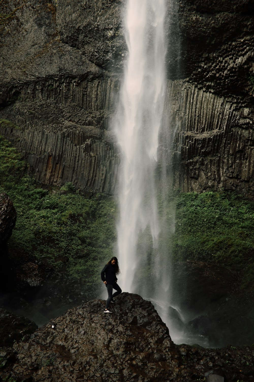 man in black shirt sitting on rock near waterfalls during daytime