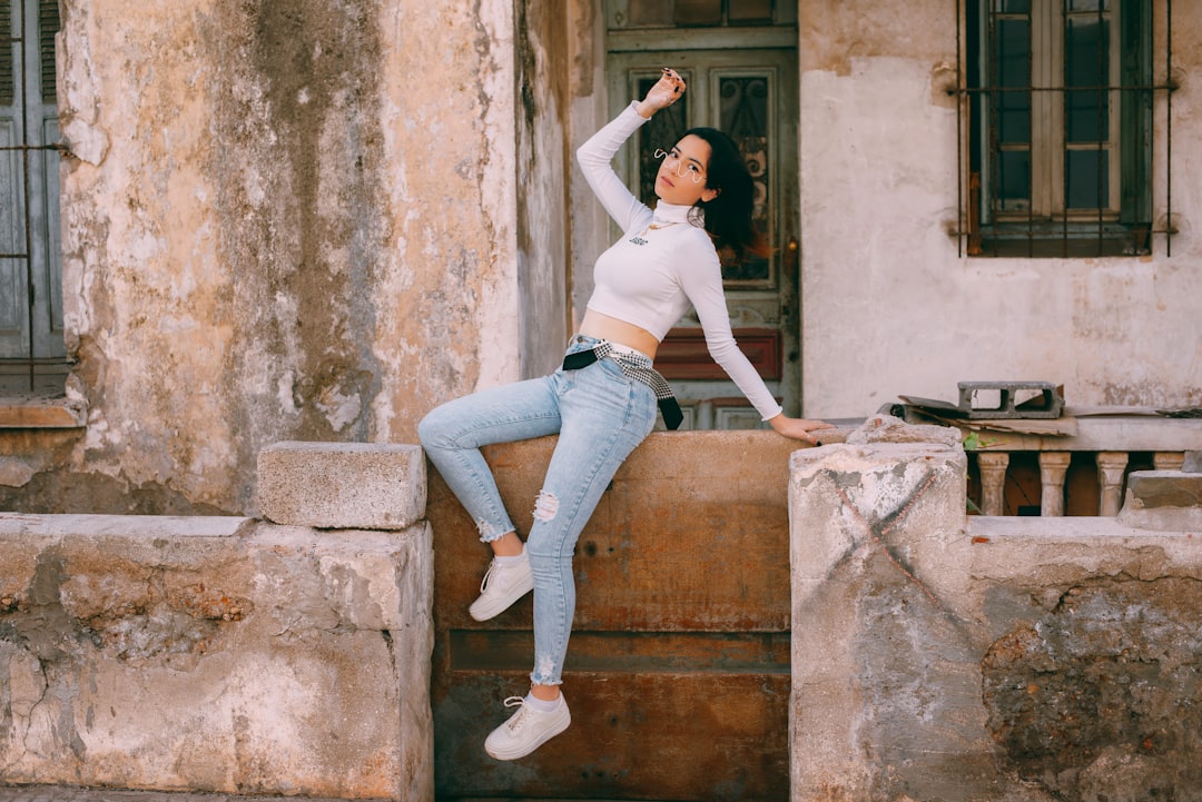 woman in white tank top and blue denim jeans standing on brown concrete stairs during daytime