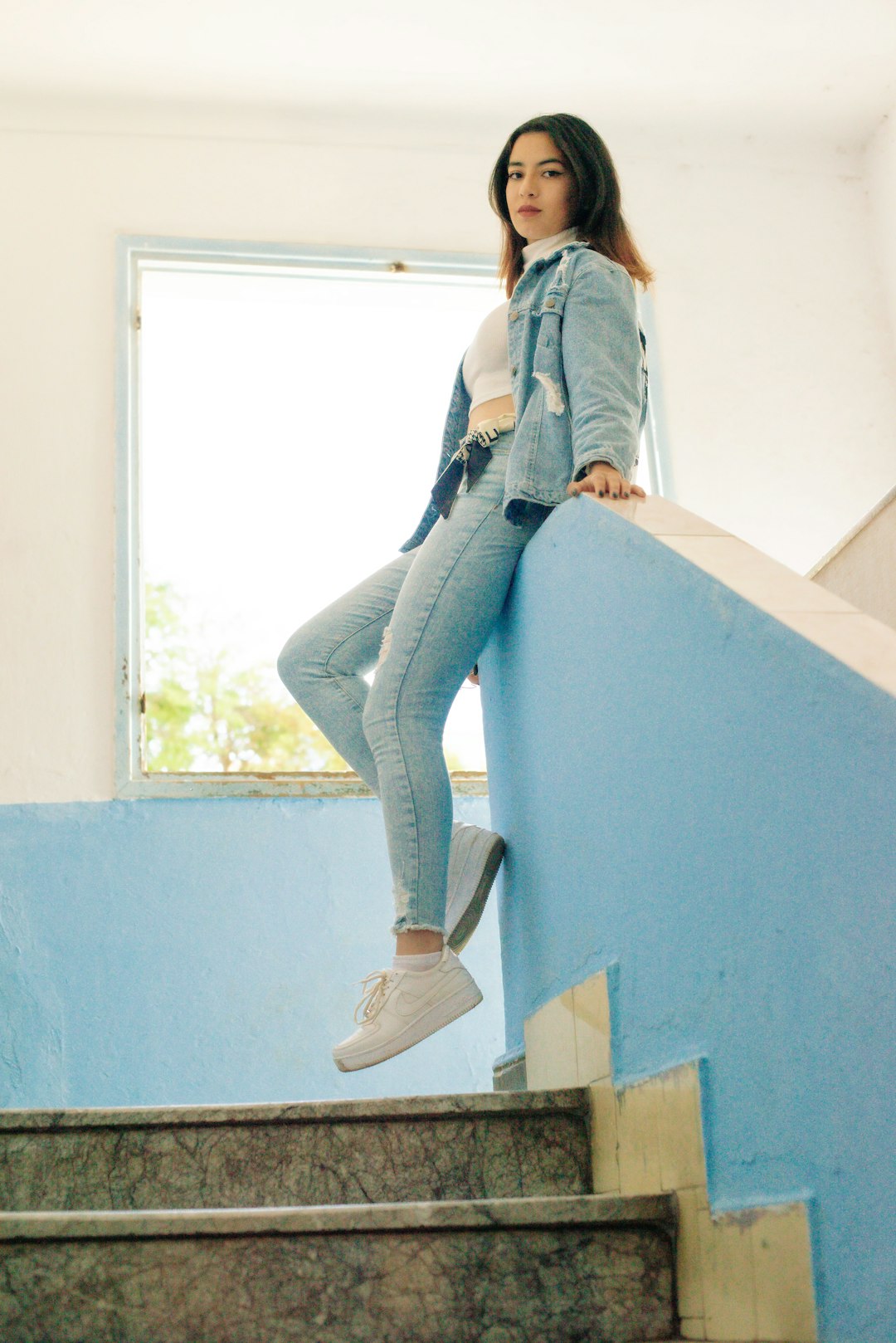 woman in blue denim jacket and blue denim jeans sitting on white concrete wall during daytime