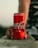 A close-up view of a hand holding a red can of Coca-Cola resting on a concrete surface. The background is blurred, drawing attention to the vibrant color and branding of the can.