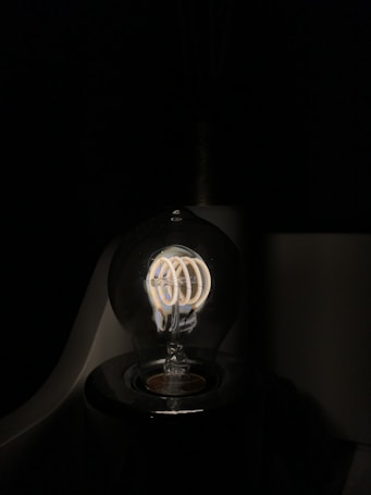 A glowing light bulb with visible coiled filament, set against a dark background, creating a stark contrast and drawing attention to the intricate details of the filament.