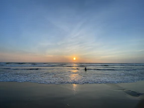 A calm Red Sea shoreline at sunset with gentle waves and a diving mask resting on the sand.