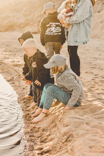 woman in brown jacket and blue denim jeans sitting on brown sand during daytime