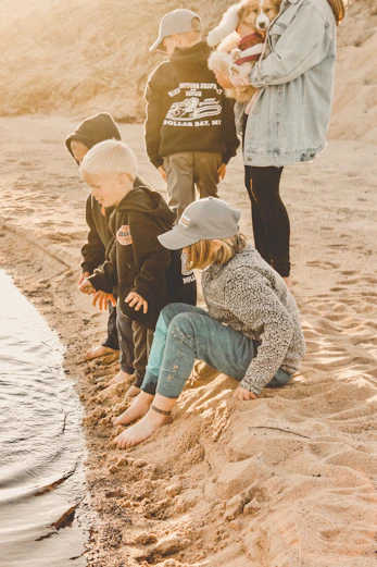 woman in brown jacket and blue denim jeans sitting on brown sand during daytime