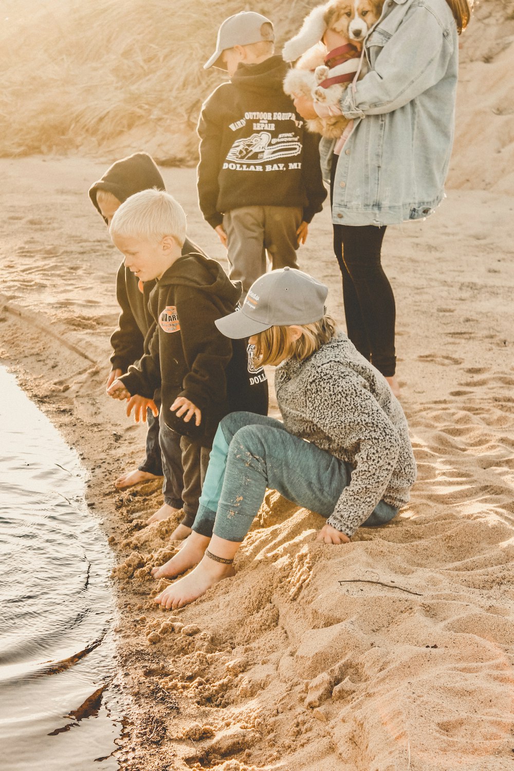 woman in brown jacket and blue denim jeans sitting on brown sand during daytime