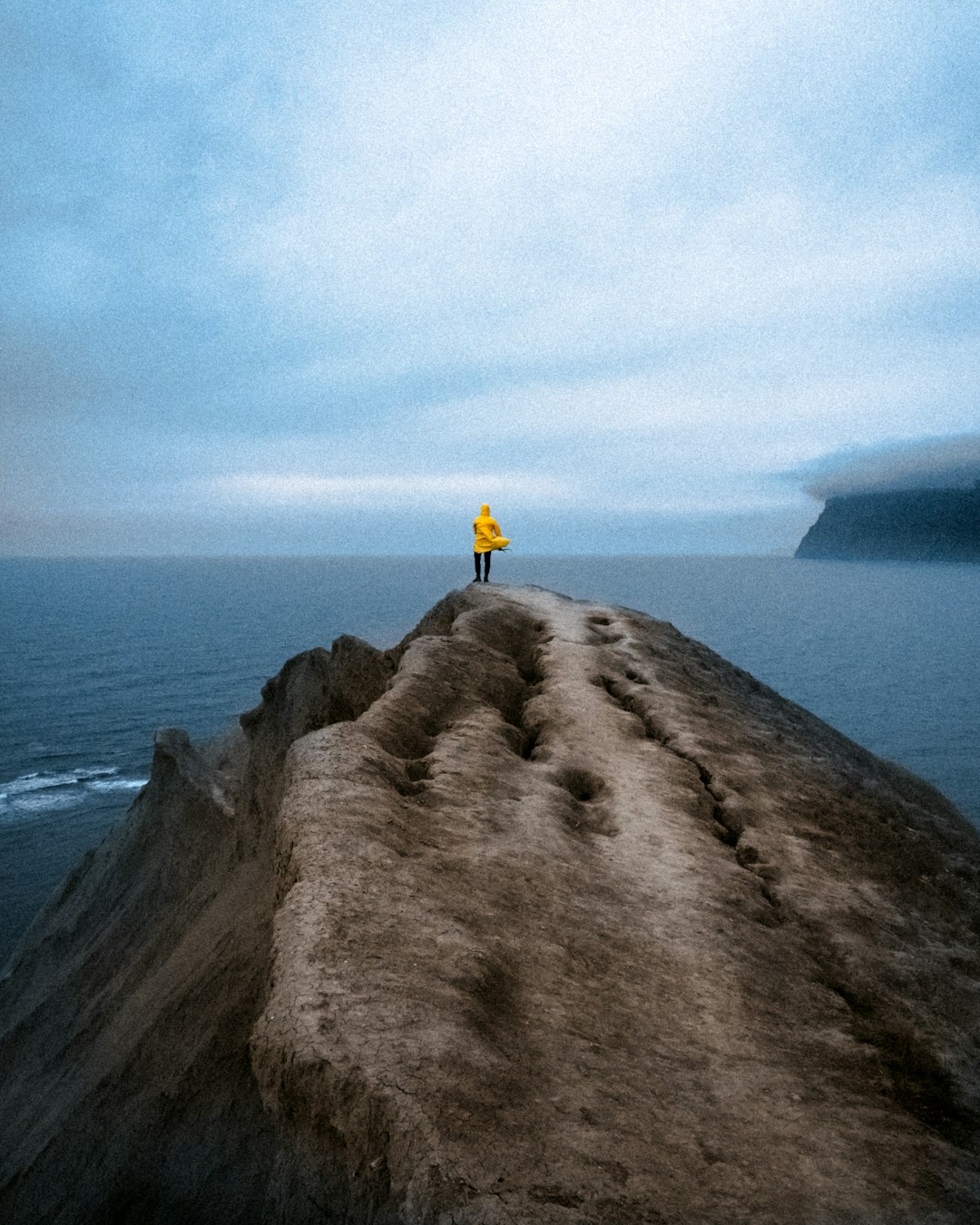person in yellow jacket standing on brown rock formation during daytime