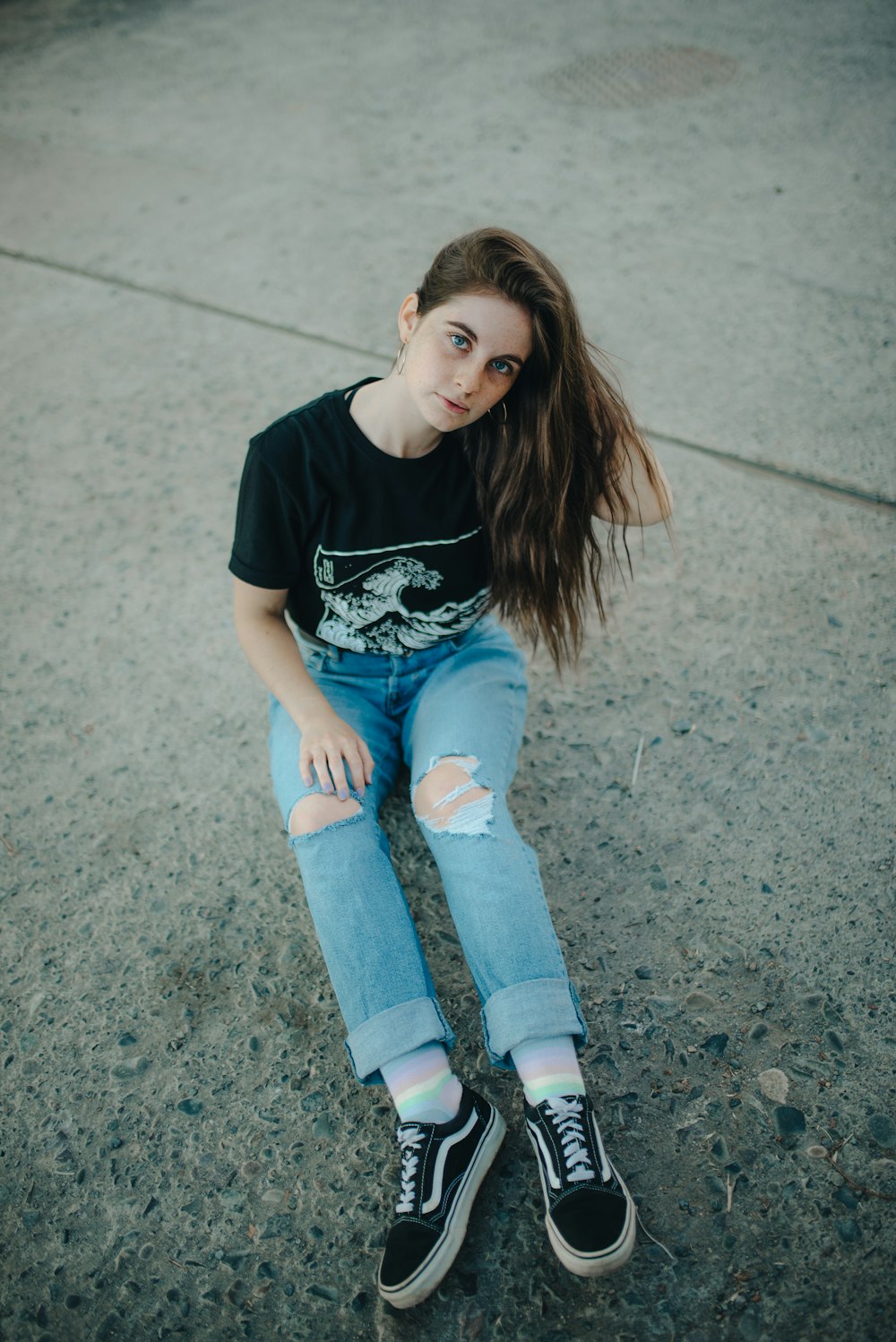 girl in black t-shirt and blue denim jeans sitting on concrete floor