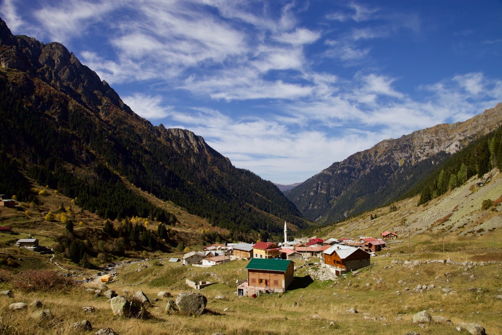 casa marrom e branca no campo de grama verde perto das montanhas sob o céu azul durante o dia