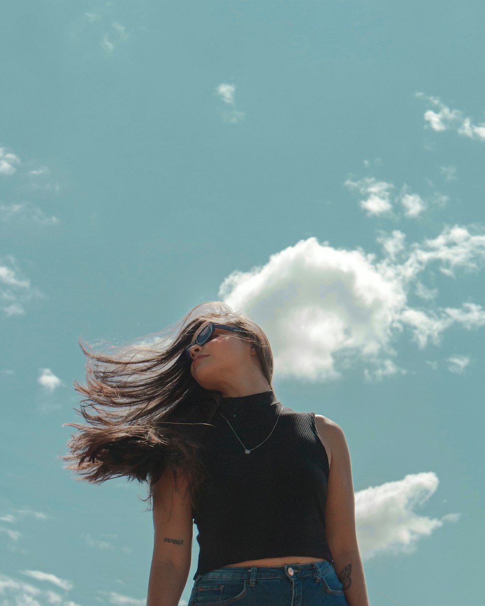 Mujer con camiseta sin mangas negra con gafas de sol bajo el cielo azul durante el día