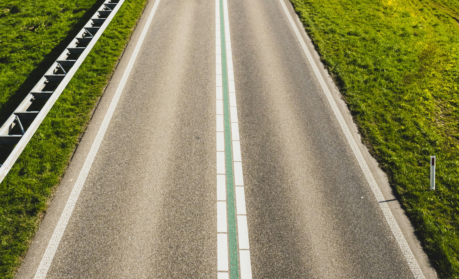 gray concrete road between green grass field during daytime
