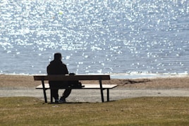 man sitting on bench near sea during daytime