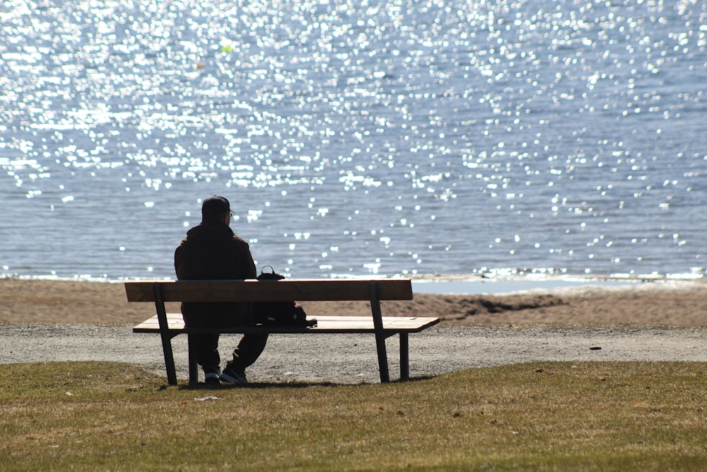 Hombre sentado en un banco cerca del mar durante el día