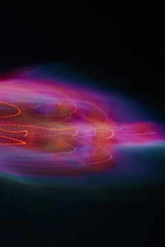 A vibrant swirl of colorful lights with hues of pink, purple, orange, and blue against a dark background. The lights form curved, dotted lines, creating an abstract pattern that appears dynamic and energetic.