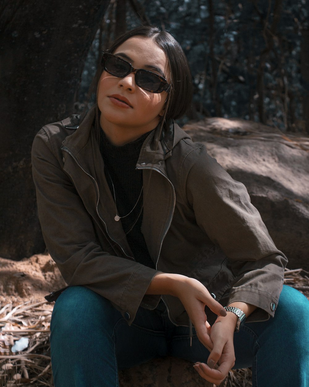 Donna in giacca marrone e jeans blu in denim che si siede sulla roccia