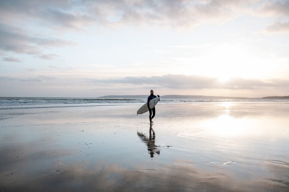 person in white long sleeve shirt and black pants walking on seashore during daytime