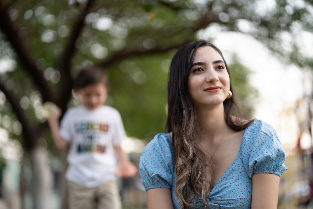 woman in blue lace dress standing near green trees during daytime