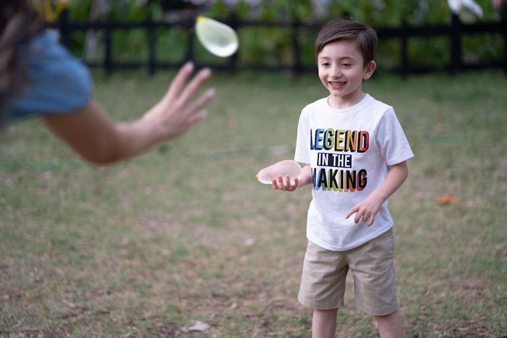 boy in white crew neck t-shirt and gray shorts standing on green grass field during