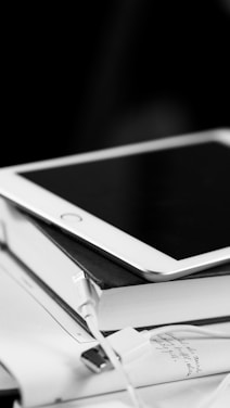 A tablet with a white bevel resting on top of several books, accompanied by a USB cable and papers with handwritten notes.
