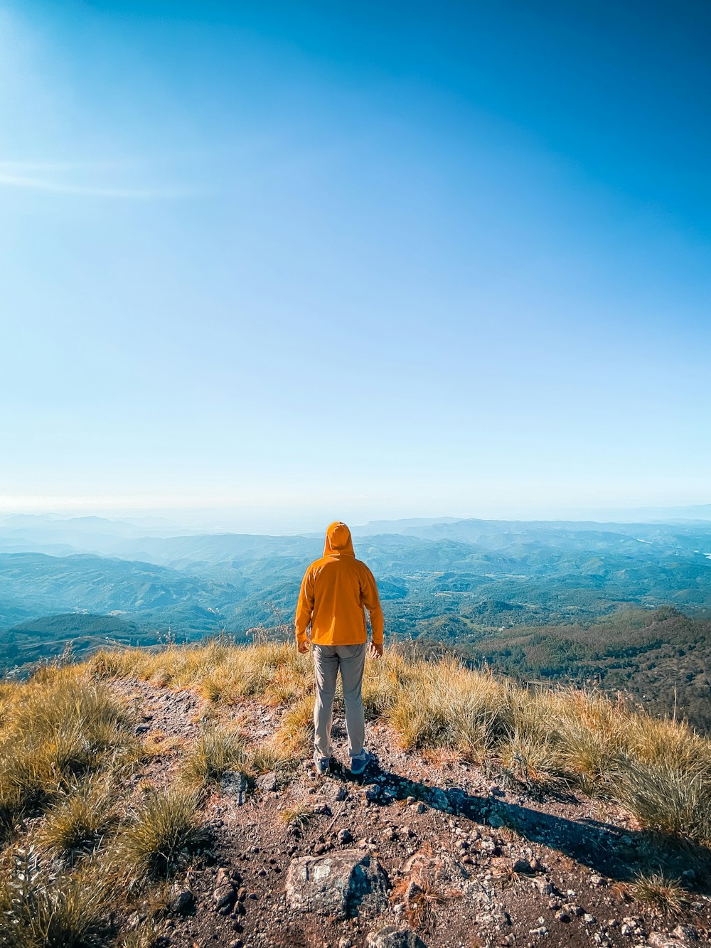 man in brown jacket standing on rocky hill during daytime