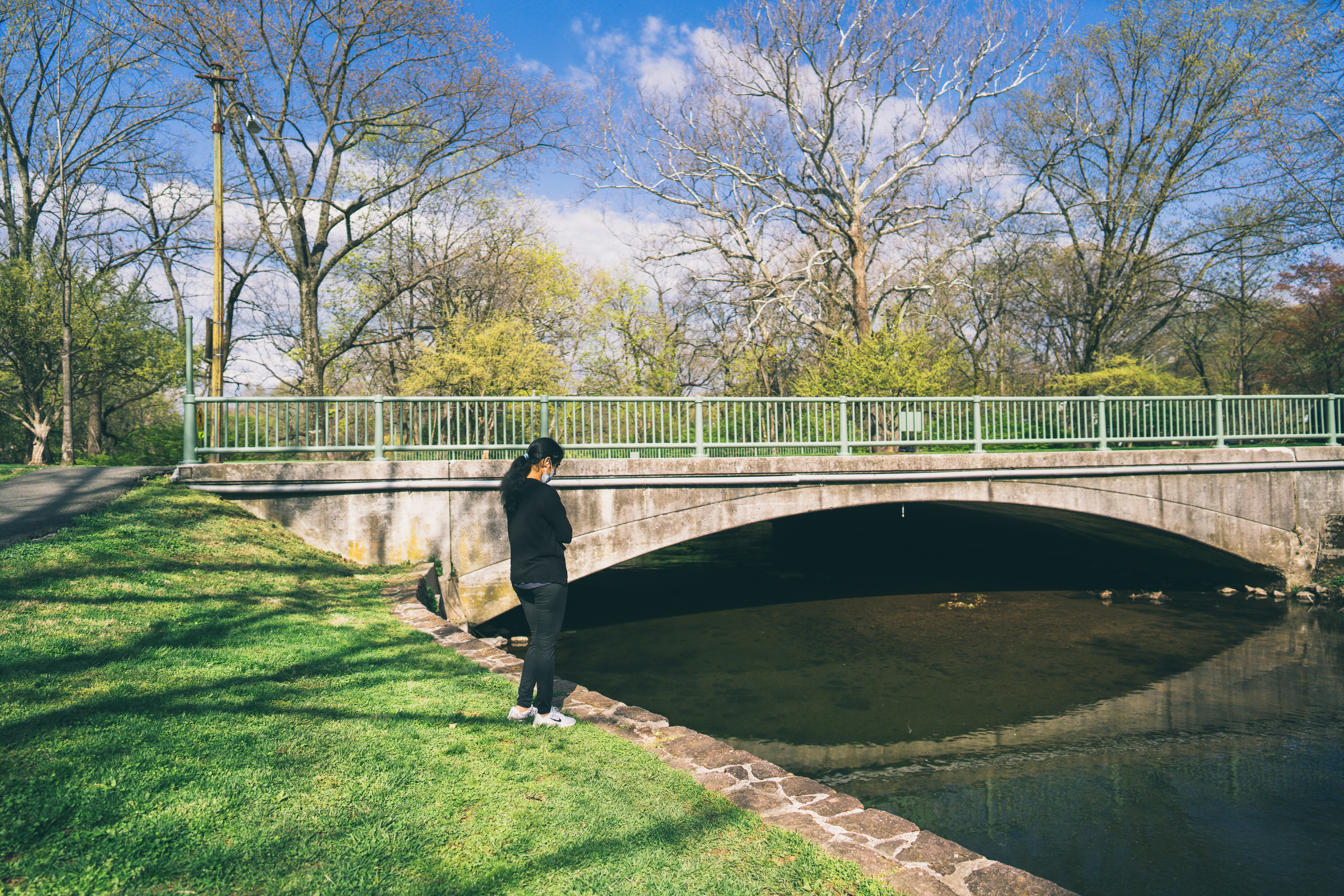 Man in black jacket and black pants standing on green grass field near bridge during daytime