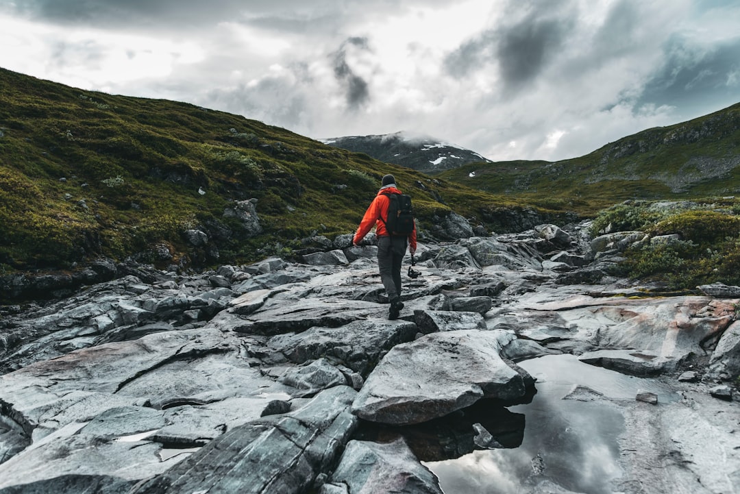 person in red jacket and black pants standing on rocky shore during daytime