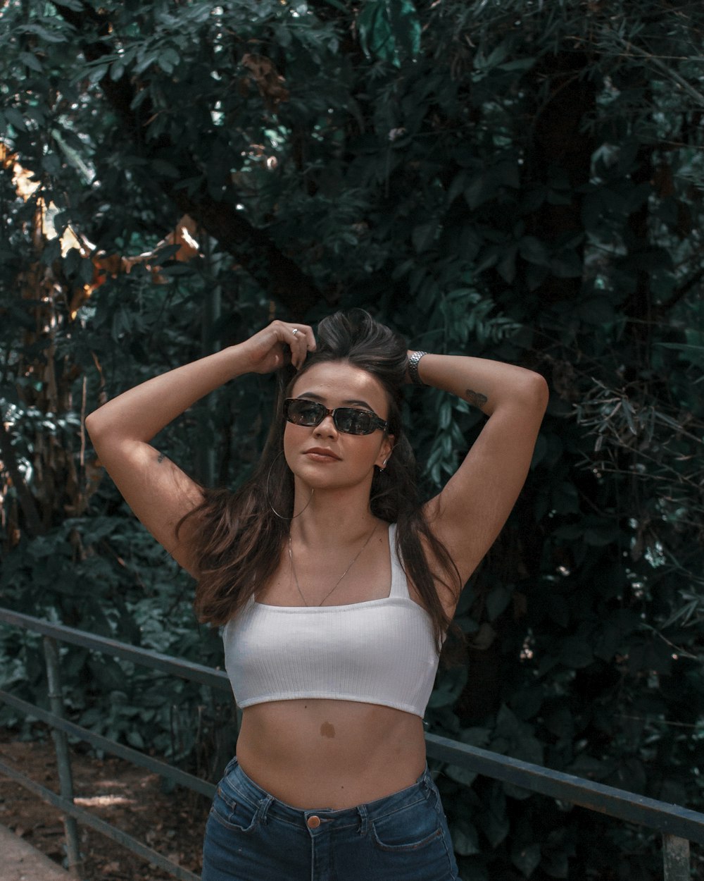 woman in white bikini top and black sunglasses standing beside green leaves during daytime