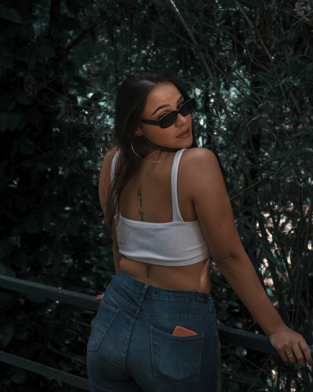 woman in white tank top and blue denim shorts standing near green leaves