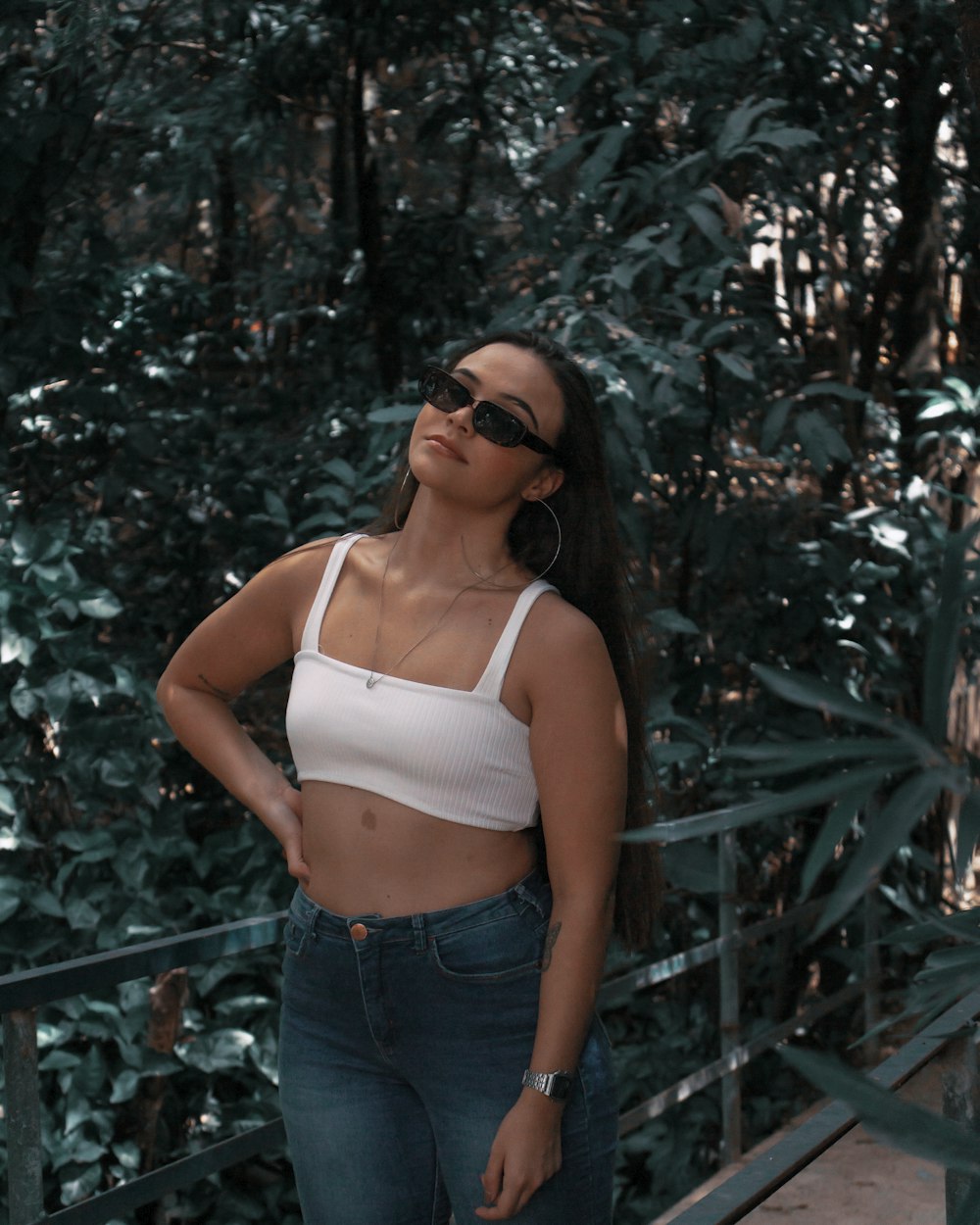 woman in white tank top and blue denim jeans standing near green leaves