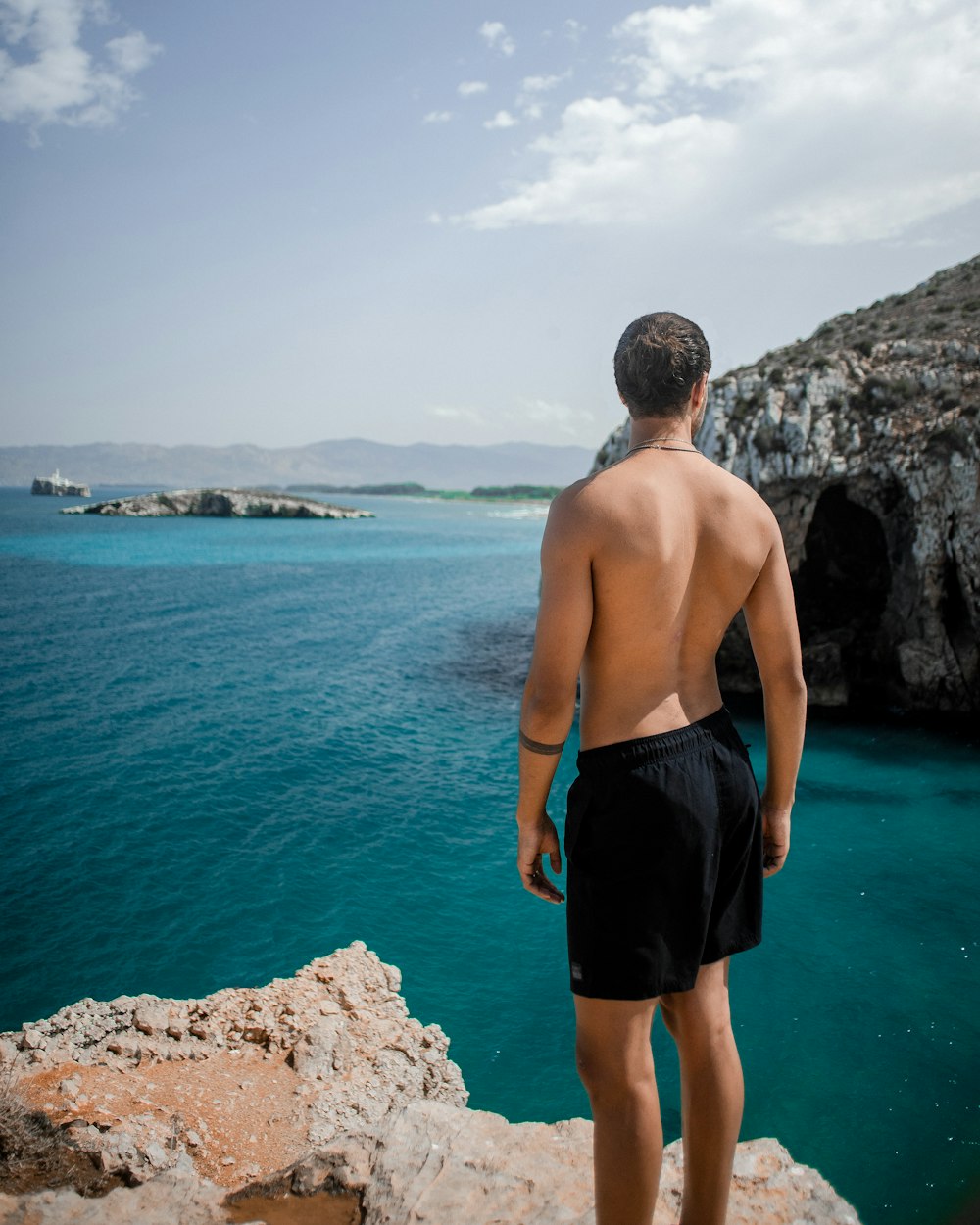 man in black shorts standing on rock formation near body of water during daytime