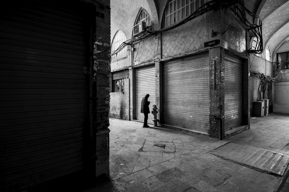 grayscale photo of man walking on sidewalk