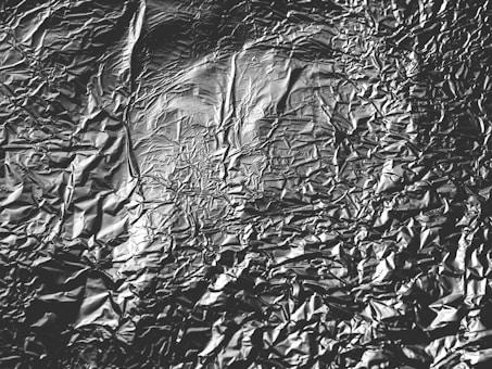 A close-up view of crumpled aluminum foil with various creases and textures creating an uneven, reflective surface.