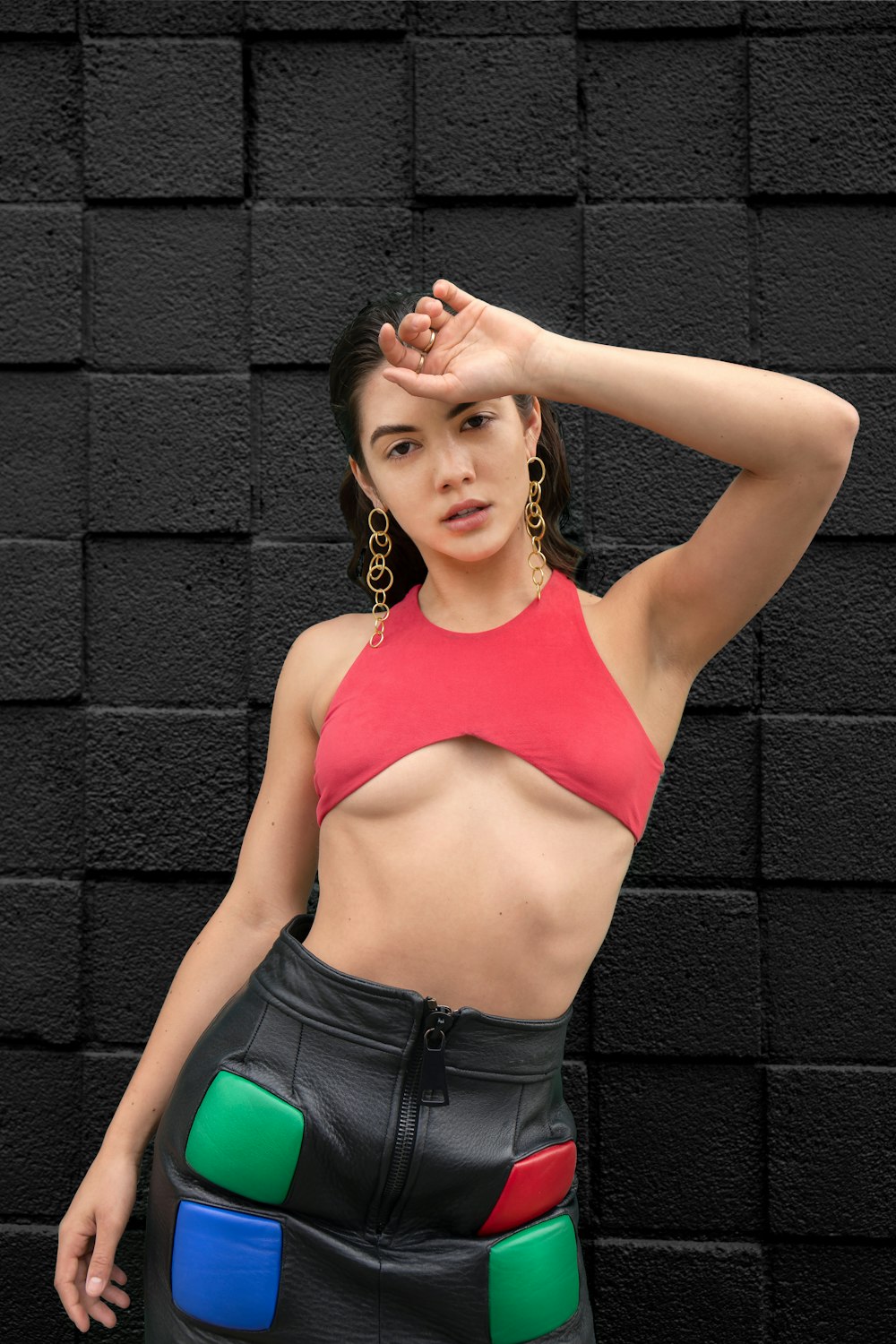 woman in pink sports bra and blue denim bottoms leaning on brick wall