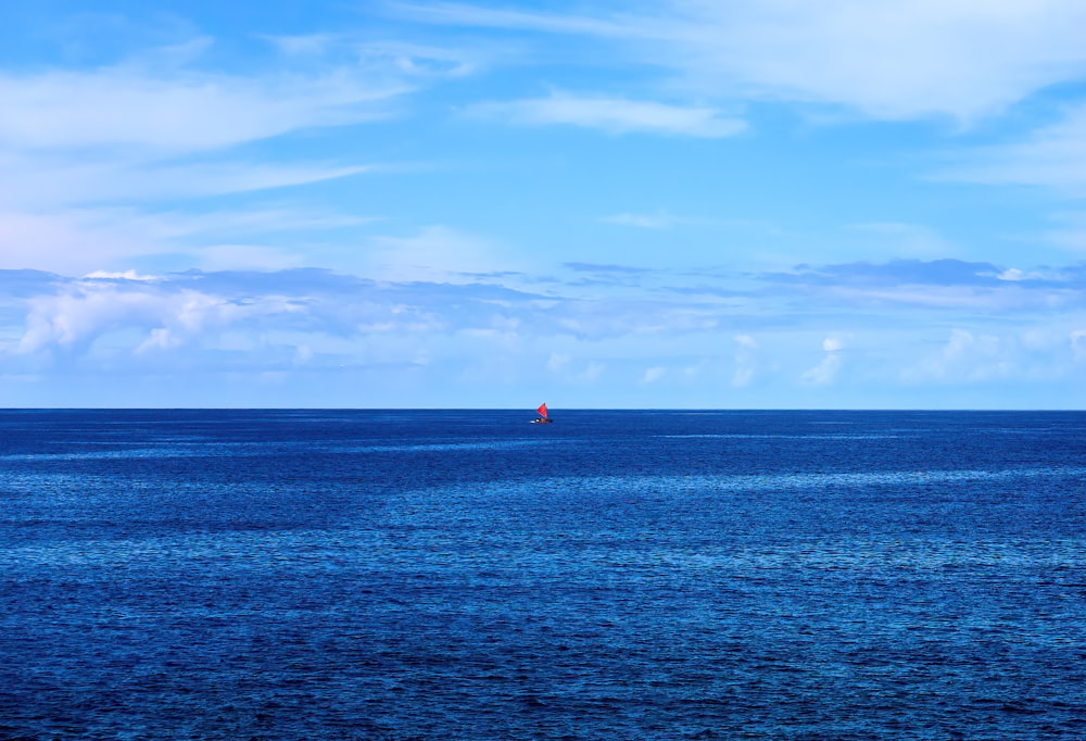 Persona con camisa roja de pie en el mar azul bajo el cielo azul durante el día