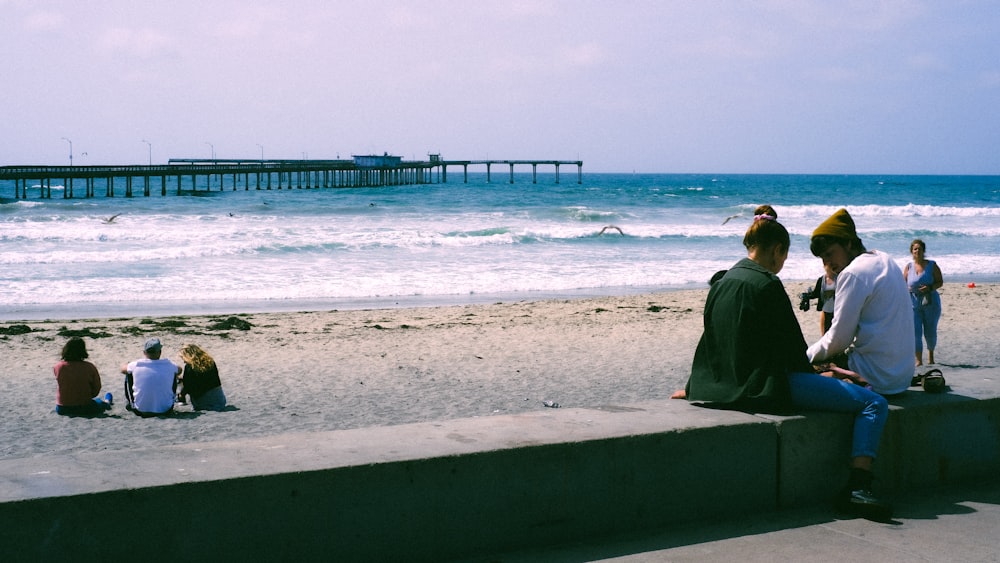 man in black hoodie sitting on concrete bench by the sea during daytime
