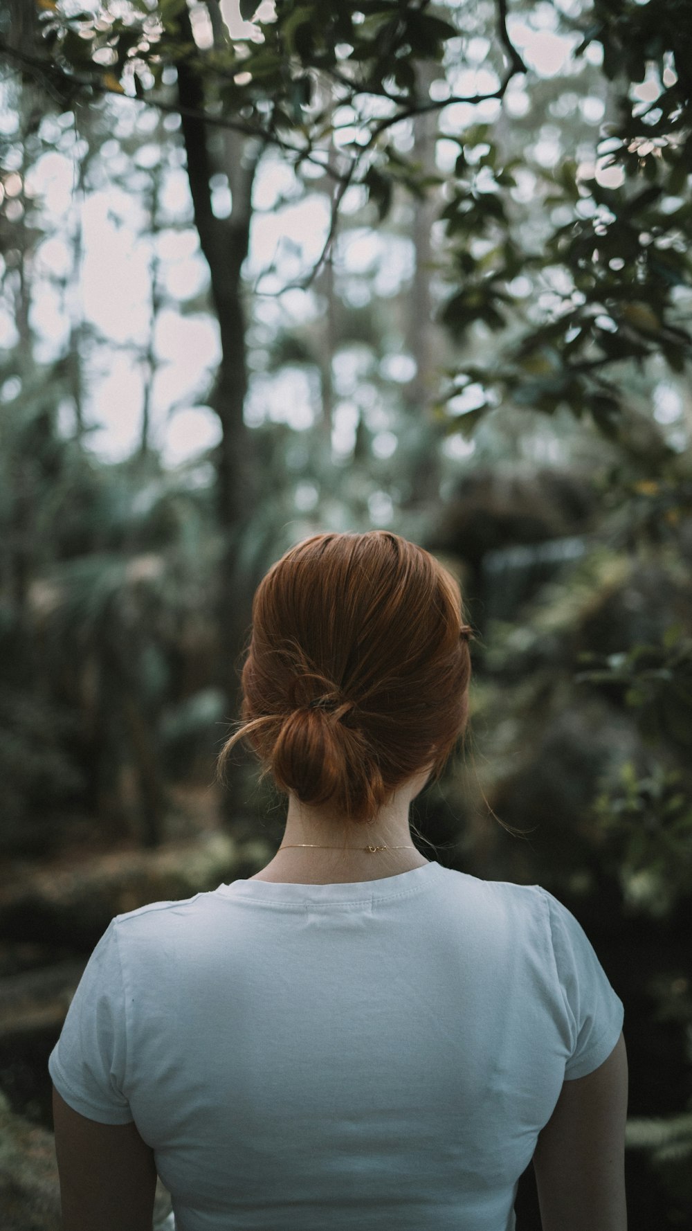 woman in white crew neck shirt standing near green trees during daytime